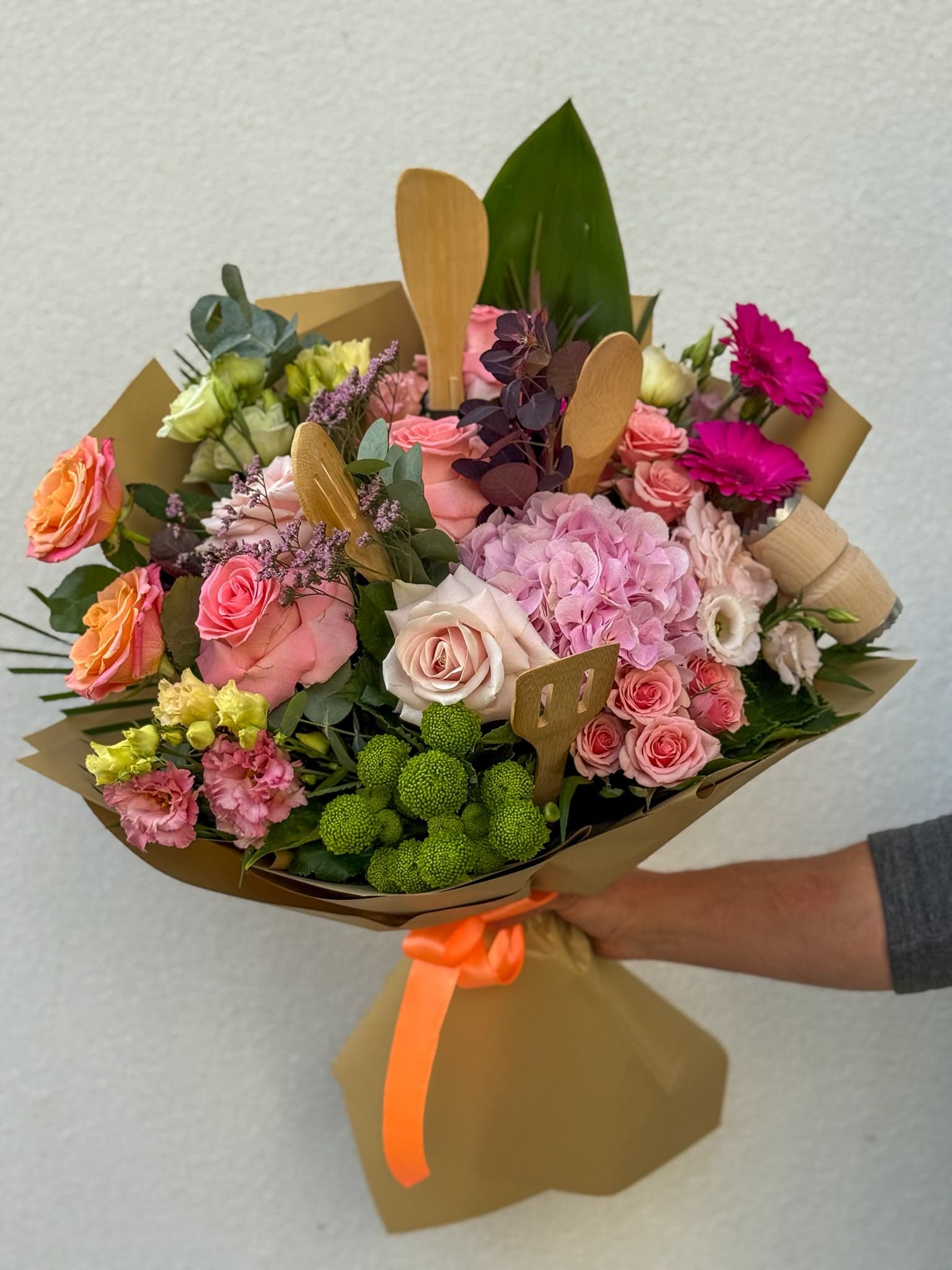 Buchet mixt de flori cu trandafiri roz, piersică și crem, hortensie roz, garoafe și flori decorative verzi, ambalat în hârtie kraft cu fundă portocalie.