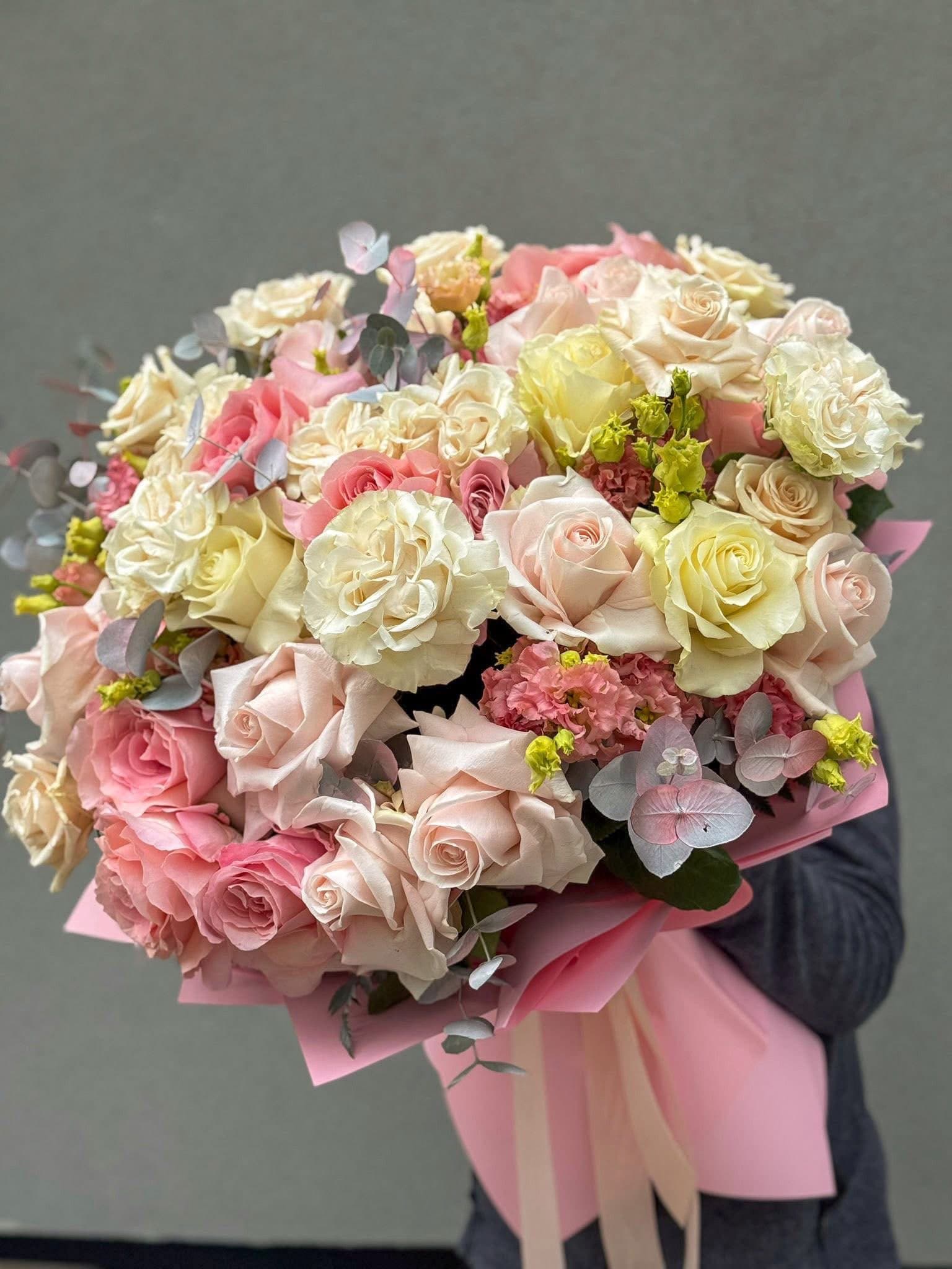 Buchet floral premium cu trandafiri roz pudrat, crem și ivoire, completat de flori decorative roz și eucalipt argintiu. Un aranjament elegant, învelit în hârtie roz pastel, ideal pentru aniversări, nunți și cadouri rafinate.